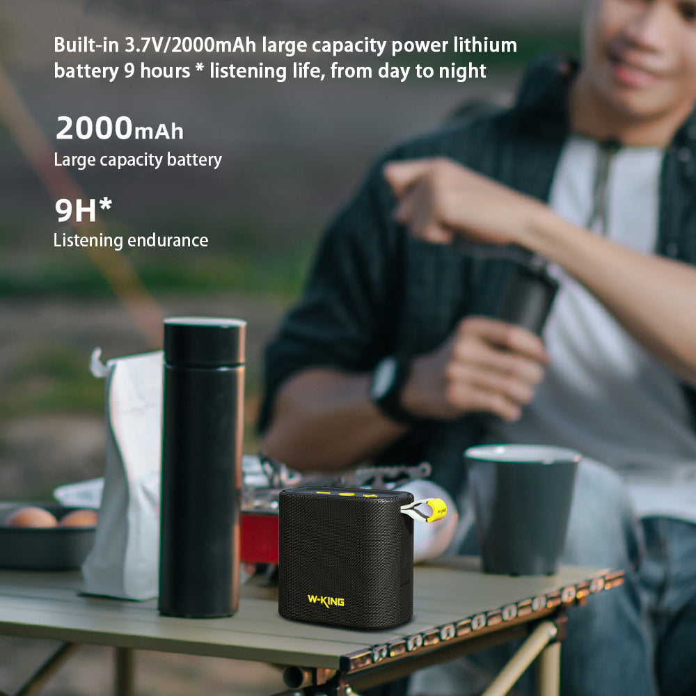 A sleek W-King D2 Bluetooth Speaker from HeadphoneHeat sits on the table with beverages and snacks. A person in the background smiles, enjoying the outdoor setting. With wireless connectivity, this compact and portable marvel offers a 2000mAh battery capacity and 9-hour listening endurance.