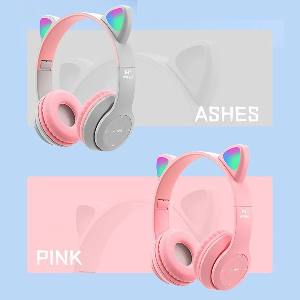 The image shows two pairs of Bluetooth VODOOL Wireless Cat Headphones with Ear Glow by HeadphoneHeat. The top pair is light grey with the "ASHES" label, and the bottom pair is pink with the "PINK" label. Both feature colorful ear accents and offer dynamic sound quality, all showcased against a light blue background.