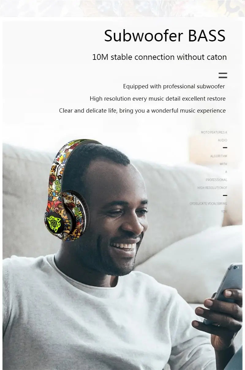 A man is smiling while wearing the vibrant Newmsnr Graffiti Foldable Wireless Bluetooth Headphones by HeadphoneHeat. He is sitting on a couch, with text above him stating "Subwoofer BASS, 10M stable connection without caton." Additional information highlights the Bluetooth 5.1 and Active Noise-Cancellation features of these headphones.