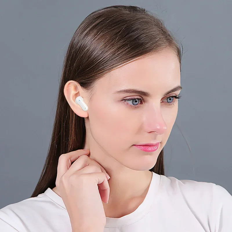 A woman with long brown hair is wearing a white t-shirt and an Esports ZIXZEX Game Bluetooth TWS Earbud by HeadphoneHeat in her right ear. She is looking to the left and holding her right hand near her chin against a plain gray background.