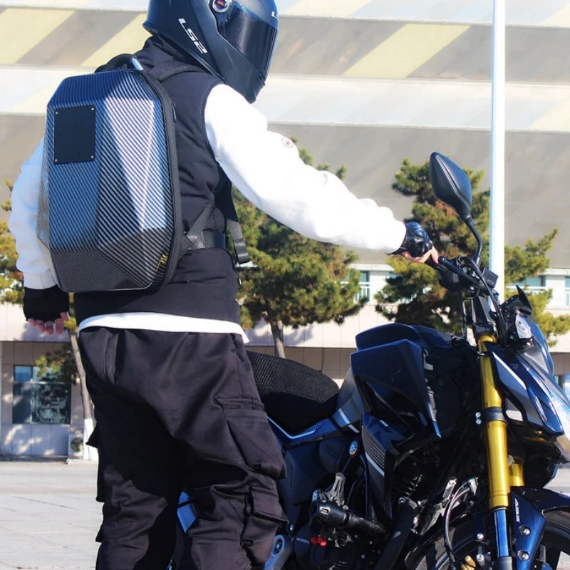 A person wearing a black helmet, white jacket, and black pants stands next to a dark blue motorcycle. They sport the CFUN LED Multimedia Business Men's Backpack by HeadphoneHeat, featuring a sleek carbon fiber design in the softback style. It's a sunny day with trees and a building in the background.