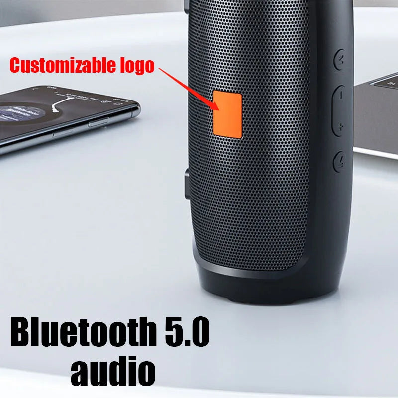 A black Portable Waterproof Subwoofer Bluetooth Speaker from HeadphoneHeat, featuring a customizable orange logo, is placed on a gray table, highlighting its portable and versatile functionality. In the background, a smartphone is visible, suggesting seamless connectivity options.