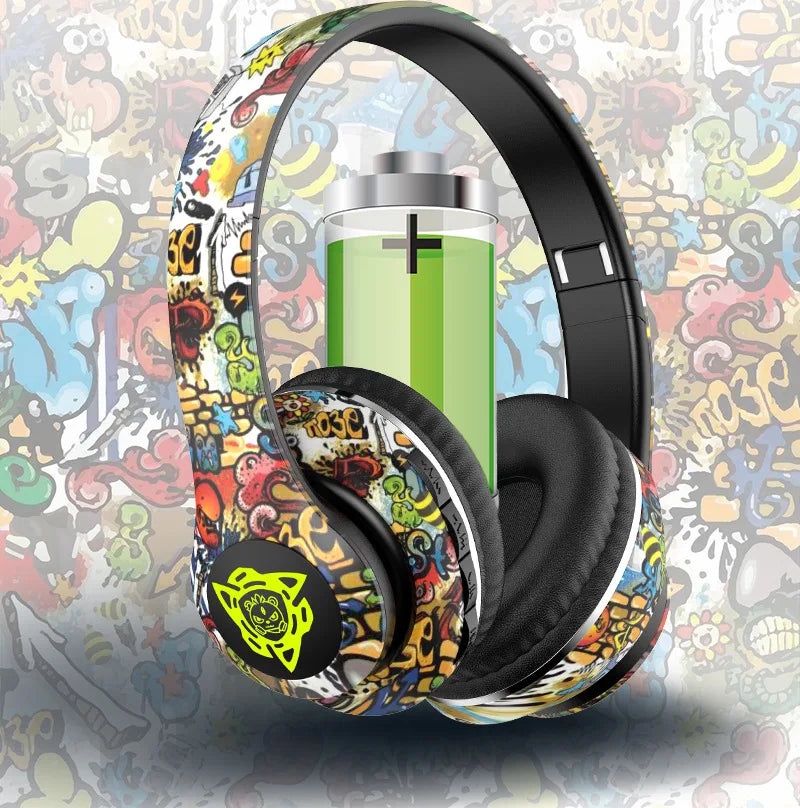 The Newmsnr Graffiti Foldable Wireless Bluetooth Headphones from HeadphoneHeat feature vibrant graffiti-style designs with a green battery icon that represents Bluetooth 5.1 connectivity on a coordinating graffiti backdrop. These headphones also incorporate active noise cancellation, skillfully merging colorful abstract patterns and characters.