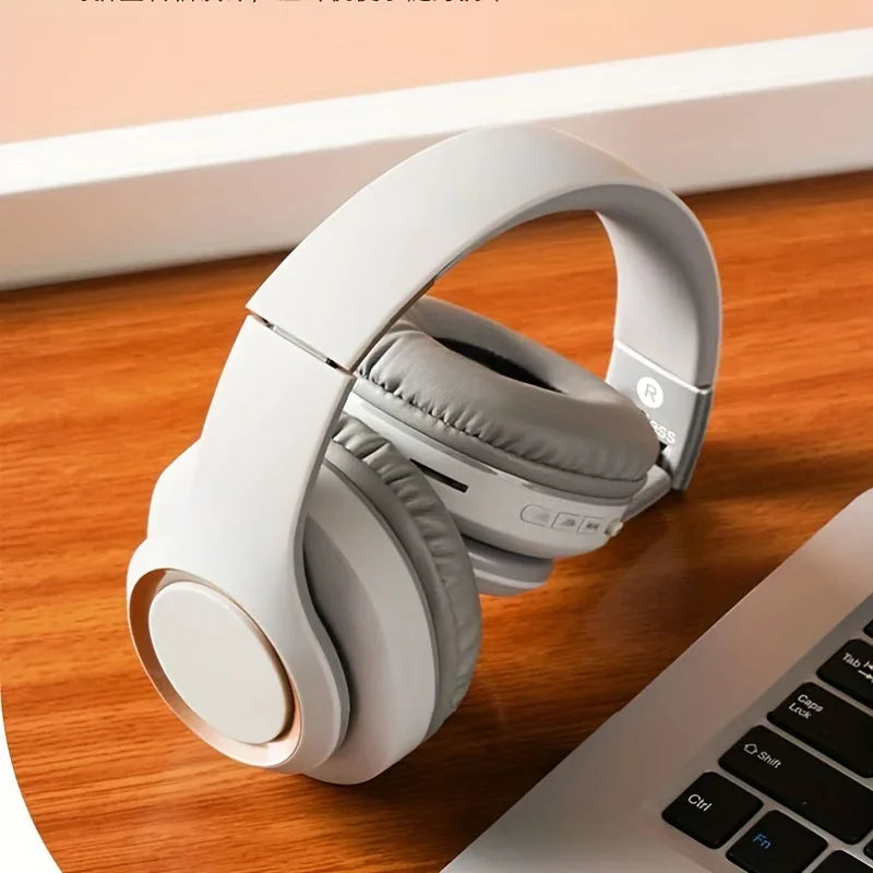 The Bluetooth HIFI Headphones Wireless Stereo by HeadphoneHeat sit on a wooden surface near a laptop, providing wireless freedom and dynamic sound quality. The scene seems to be set on a desk with a warm-colored wall in the background.