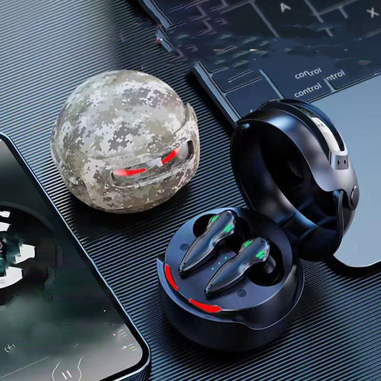 A set of HeadphoneHeat Fortipod Wireless Neutral Noise Cancellation Gaming Earbuds with charging cases. One case is black and open, revealing the earbuds boasting Bluetooth protocol 5.3 for seamless connection. The other case is closed with a camouflage pattern, known for its long battery life. Nearby are a smartphone displaying graphics and the keyboard of a laptop, all on a dark surface.